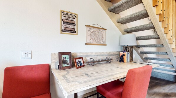 A dining area with a rustic wooden table, red chairs, framed pictures, and a map on the wall.