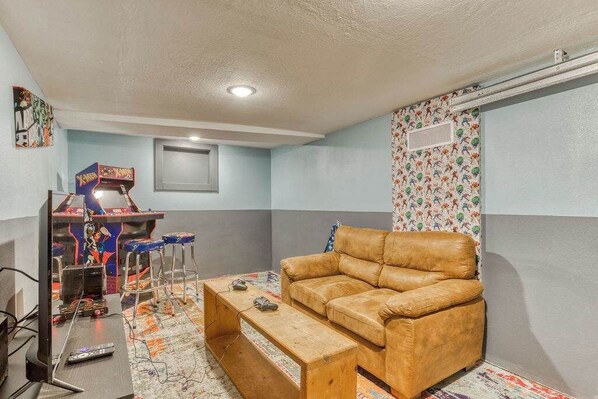 A room with a brown leather sofa, a wooden coffee table, a gaming console, and a patterned wall.