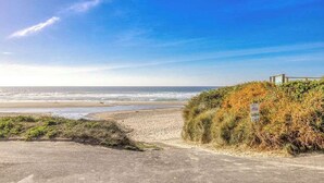 Una carretera costera con una playa a la derecha, cielo despejado y una señal.