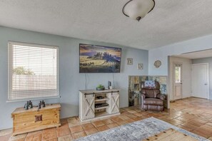 Ein Wohnzimmer mit großem Fenster, einem aufgehängten Gemälde, einem Ledersessel und einem Holzkabinett.