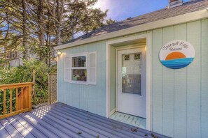 A small, light blue building with a wooden deck, a door, and a sign that reads 'Frugal Edge Retreat.'