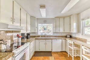 A kitchen with white cabinets, a stove, a sink, and a window.