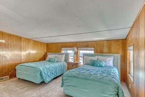 A bedroom with two beds, wooden walls, a window, and a nightstand.