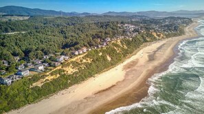 Ein Küstenwohngebiet mit Häusern entlang eines Sandstrandes und einem bewaldeten Hügelhang.