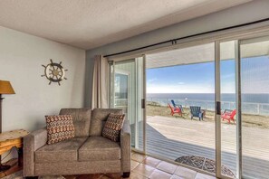 A room with a sofa, a wall clock, and a view of the beach through a sliding glass door.