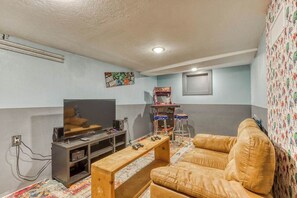 Una sala de estar con televisor, una mesa de centro de madera, un sofá de cuero y una consola de videojuegos.