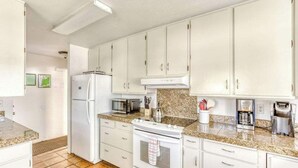 Una cocina con gabinetes blancos, refrigerador, microondas, estufa y cafetera.
