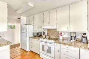 Una cocina con gabinetes blancos, refrigerador, microondas, estufa y cafetera.