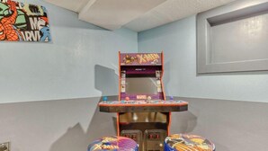 Una habitación con una máquina recreativa de tema Marvel X-Men, dos taburetes con diseños a juego y un cartel colgado en la pared.