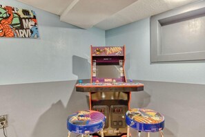 Una habitación con una máquina recreativa de tema Marvel X-Men, dos taburetes con diseños a juego y un cartel colgado en la pared.