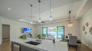 Une cuisine moderne dotée d’un grand îlot central, d’appareils électroménagers intégrés et de luminaires suspendus.