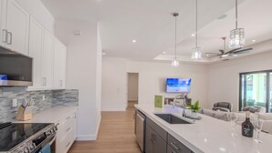 Une cuisine moderne dotée d’un grand îlot central, d’appareils électroménagers en acier inoxydable et d’un téléviseur à écran plat.