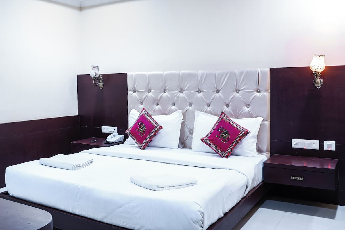 A neatly made bed with white linens and two decorative pillows, a bedside table with a phone, and a nightstand with a lamp.