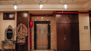 Un ascenseur doté d’une poignée rouge, d’un miroir décoratif et d’une statue posée sur un piédestal.