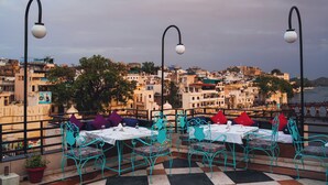 Une terrasse avec des sièges, des tables et des lampadaires, offrant une vue sur un paysage urbain avec des bâtiments et une rivière.