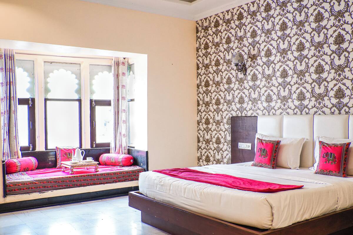A bedroom with a large bed, a window with curtains, and patterned wallpaper.