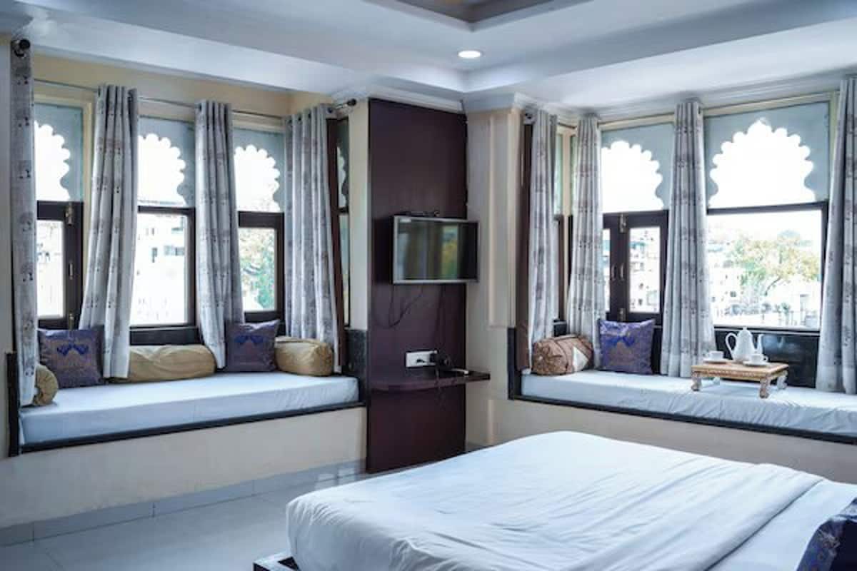 A hotel room with two beds, a television, and windows with decorative curtains.