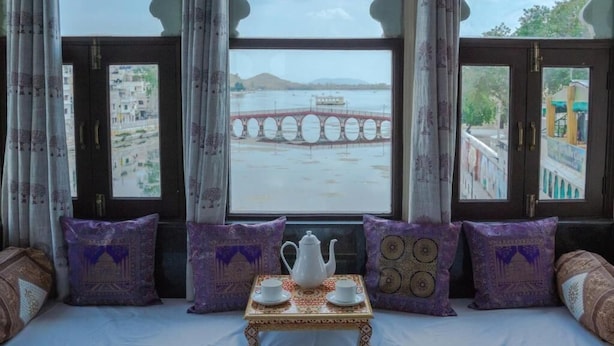 Une pièce avec un lit, une table sur laquelle se trouvent une théière et des tasses, et une vue sur un pont et sur l’eau.