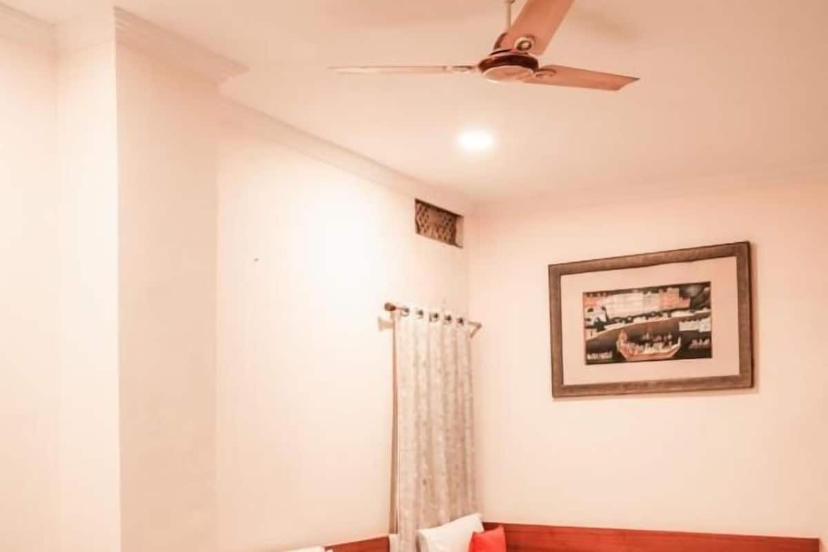 A hotel room with three beds, a ceiling fan, a framed picture on the wall, and a curtain.