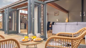 An open patio with wicker chairs, a breakfast table with croissants and juice, and a view into the interior of a modern home.