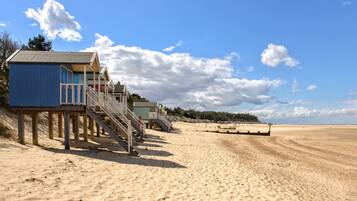 A beach with wooden structures, including a blue building with stairs and a green building with a sign.