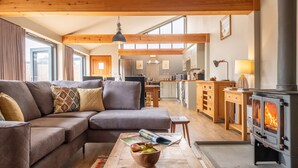 A modern living room with a sectional sofa, a wooden coffee table with fruits, a magazine, and a wood-burning stove.