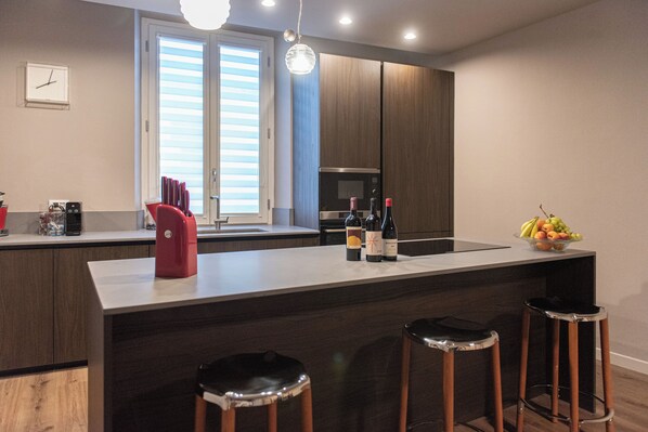 A modern kitchen with a central island, bar stools, a microwave, and a fruit bowl. - Relaxation and design in the center of Lucca (Lucca)