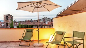 Terrassa amb dues cadires plegables verdes i un gran parasol, amb vista a una vila amb edificis històrics i una torre.