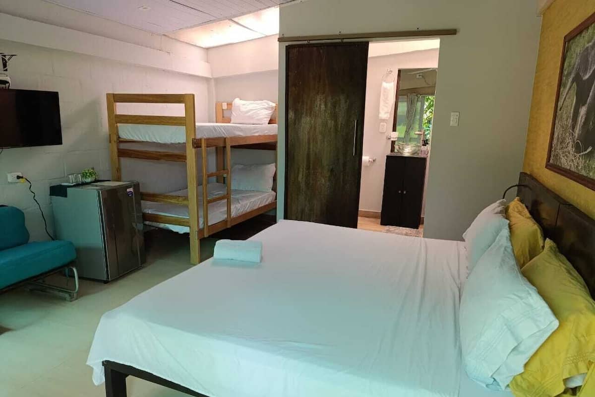 A bedroom with a large bed, a bunk bed, a desk, a chair, and a TV.