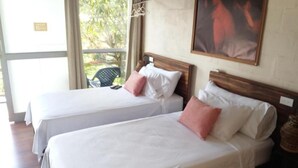 Two single beds with white linens and pink pillows, a wooden headboard, a painting on the wall, and a window with a view of greenery. - Amazonas Explorers Leticia (Leticia)