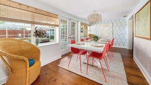 Un coin repas avec une table blanche, des chaises rouges et un fauteuil en osier.