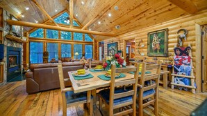 Interior de una cabaña de troncos con chimenea, una mesa de comedor de madera y un rincón de estar acogedor.