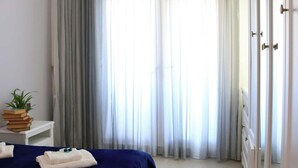 A bedroom with a bed, a nightstand with a plant and books, a dresser, and a large window with curtains. - Kristal Absheron 110 (Baku)