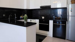 A modern kitchen with black countertops, white cabinets, a stainless steel refrigerator, and a small potted plant. - Kristal Absheron 110 (Baku)