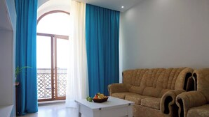 A living room with a sofa, a coffee table, and a balcony with blue curtains. - Kristal Absheron 110 (Baku)