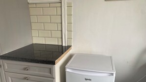 Una kitchenette con un refrigerador blanco, una encimera negra y un armario blanco con cajones.