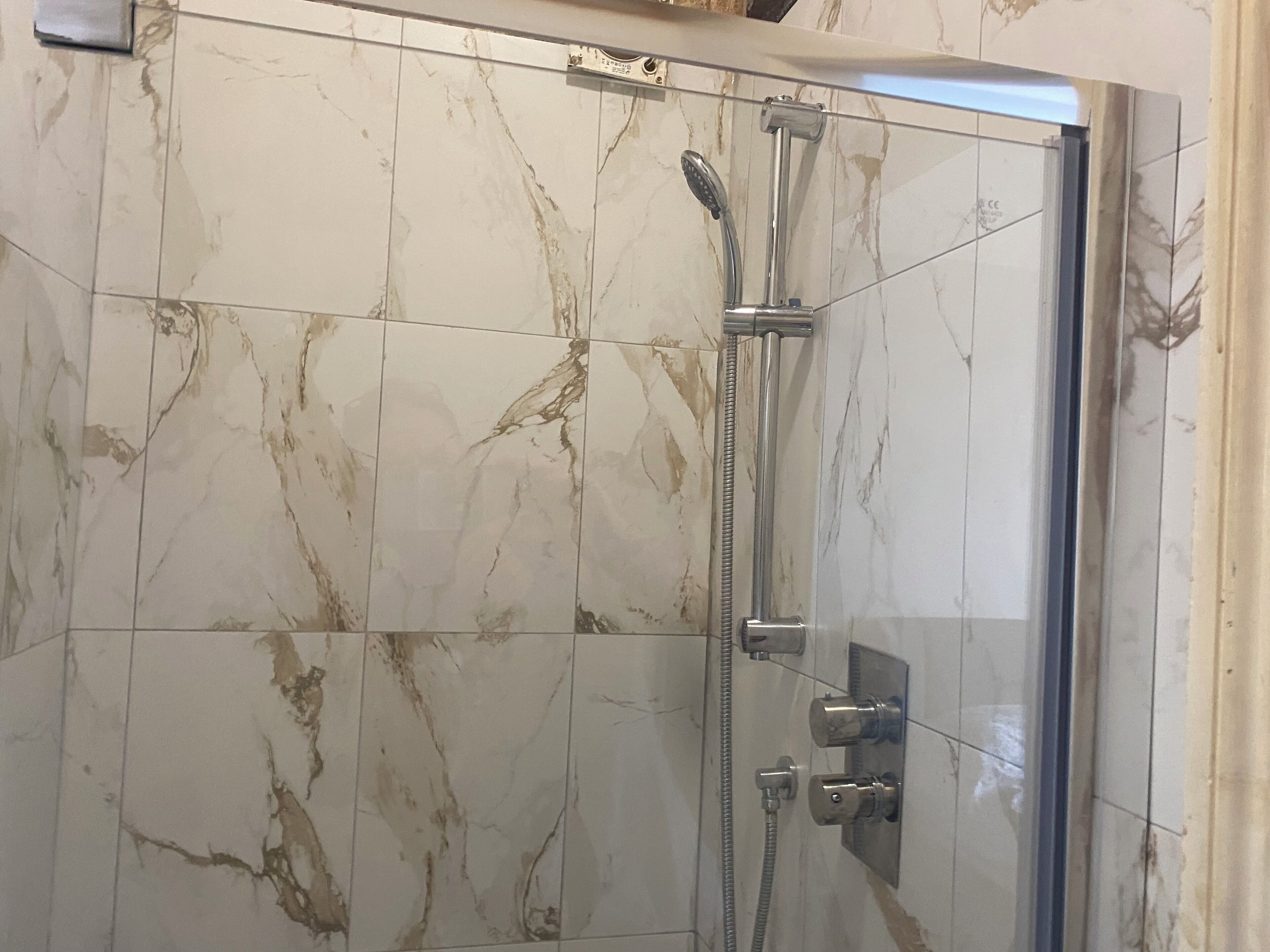 A glass-enclosed shower with a handheld showerhead and a wall-mounted control panel.