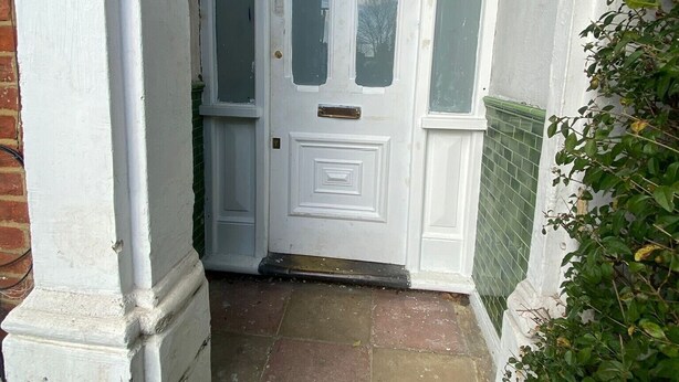 Una puerta blanca con un panel decorativo, un ventanal pequeño y un timbre.