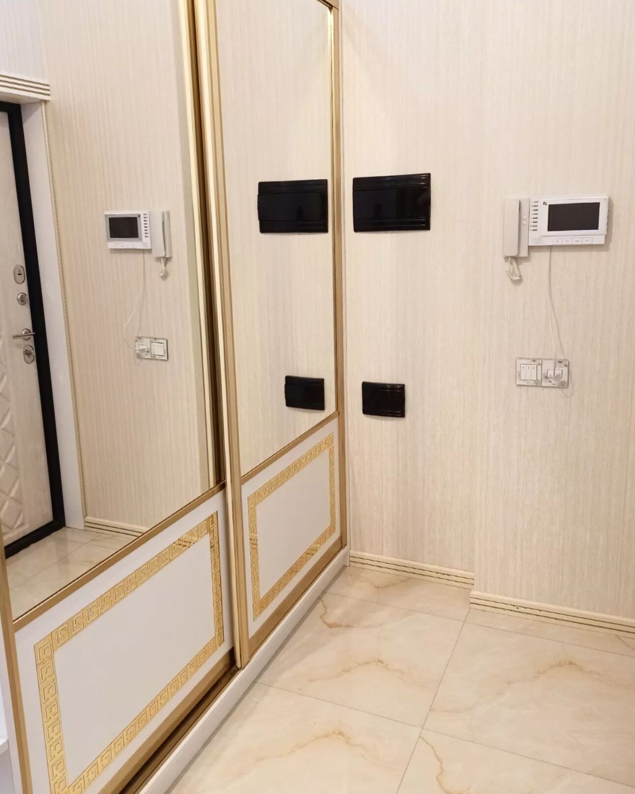 A room with a large mirror, a wardrobe with a gold trim, and a tiled floor.