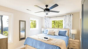 Un dormitorio con cama, ventilador de techo, mesita de noche y ventana con cortinas.