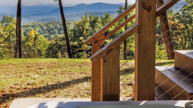 Un jacuzzi con una escalera de madera que lleva a una terraza, rodeado de árboles y un paisaje montañoso.