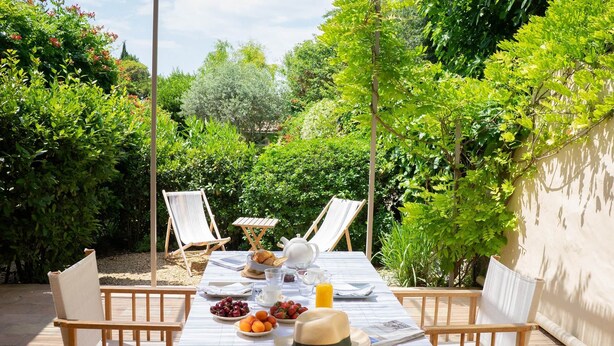 A table set outdoors with a view of lush greenery, two chairs, a tablecloth, and a hat. - Apartment les canisses (UZES)