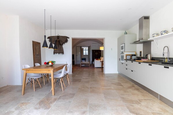 A modern kitchen with white cabinets, a central island, and a dining area with a wooden table and chairs. - Apartment les canisses (UZES)
