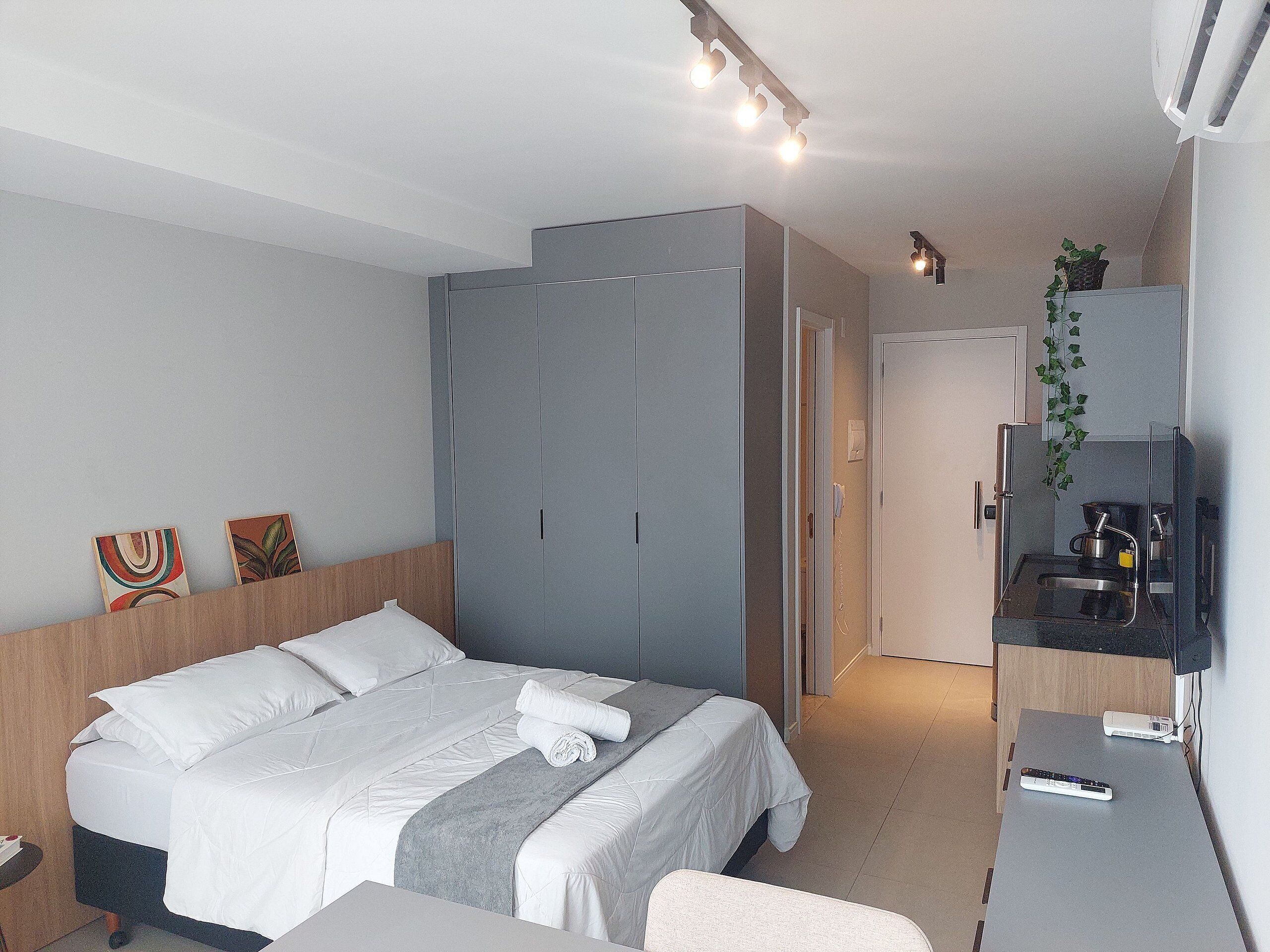 A modern bedroom with a bed, a wardrobe, a small kitchenette, and a television.