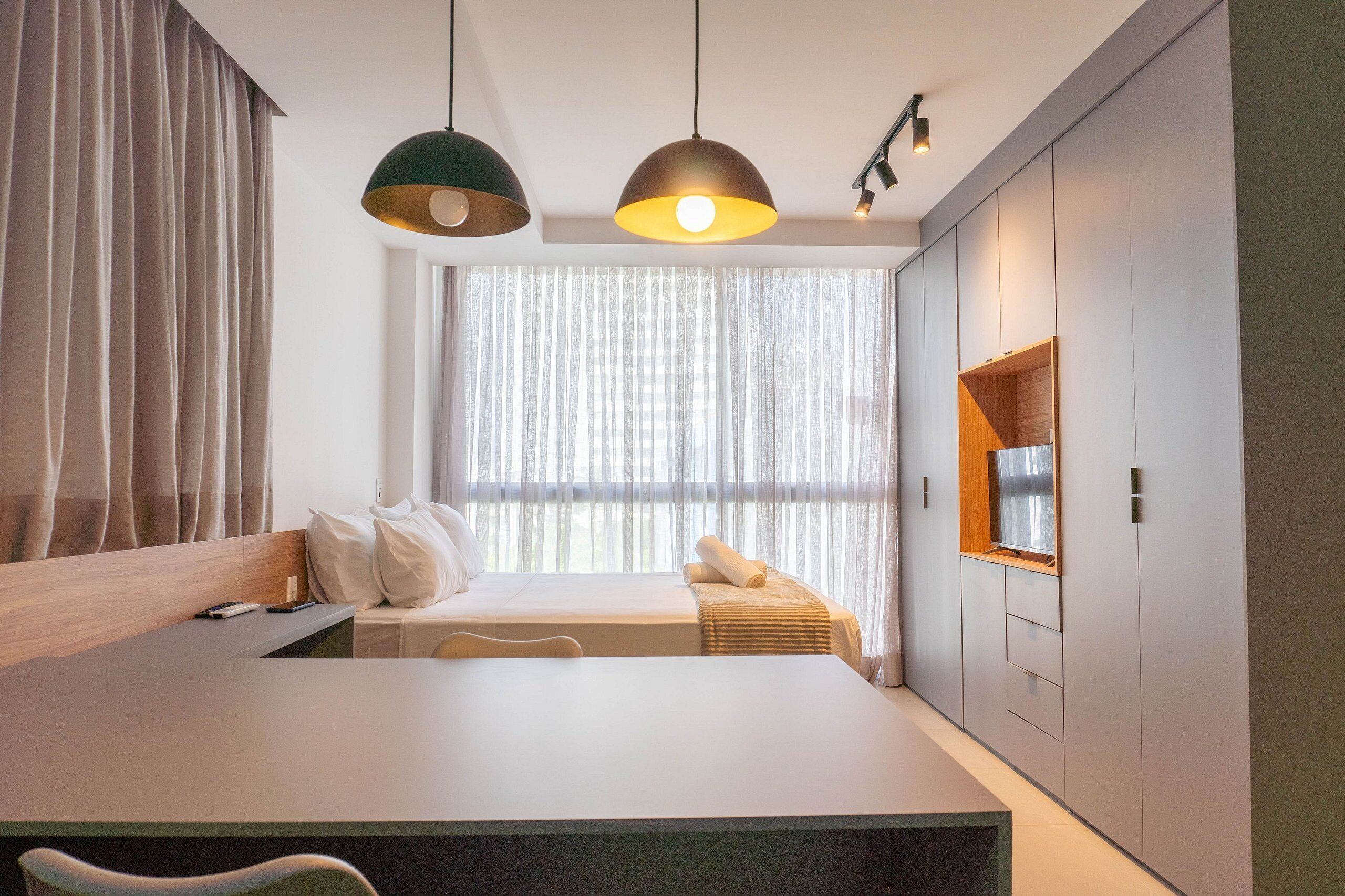 A modern hotel room with a large bed, a desk, and a TV shelf.