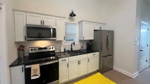Una cocina con armarios blancos, microondas, estufa y refrigerador.