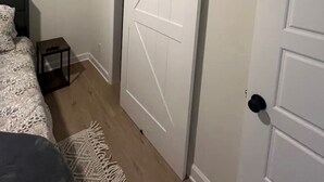 Un dormitorio con una cama, una mesita de noche pequeña, una puerta blanca y una puerta corredera de estilo rústico.