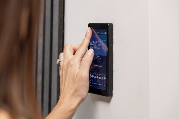 Une main interagissant avec un thermostat numérique fixé au mur.