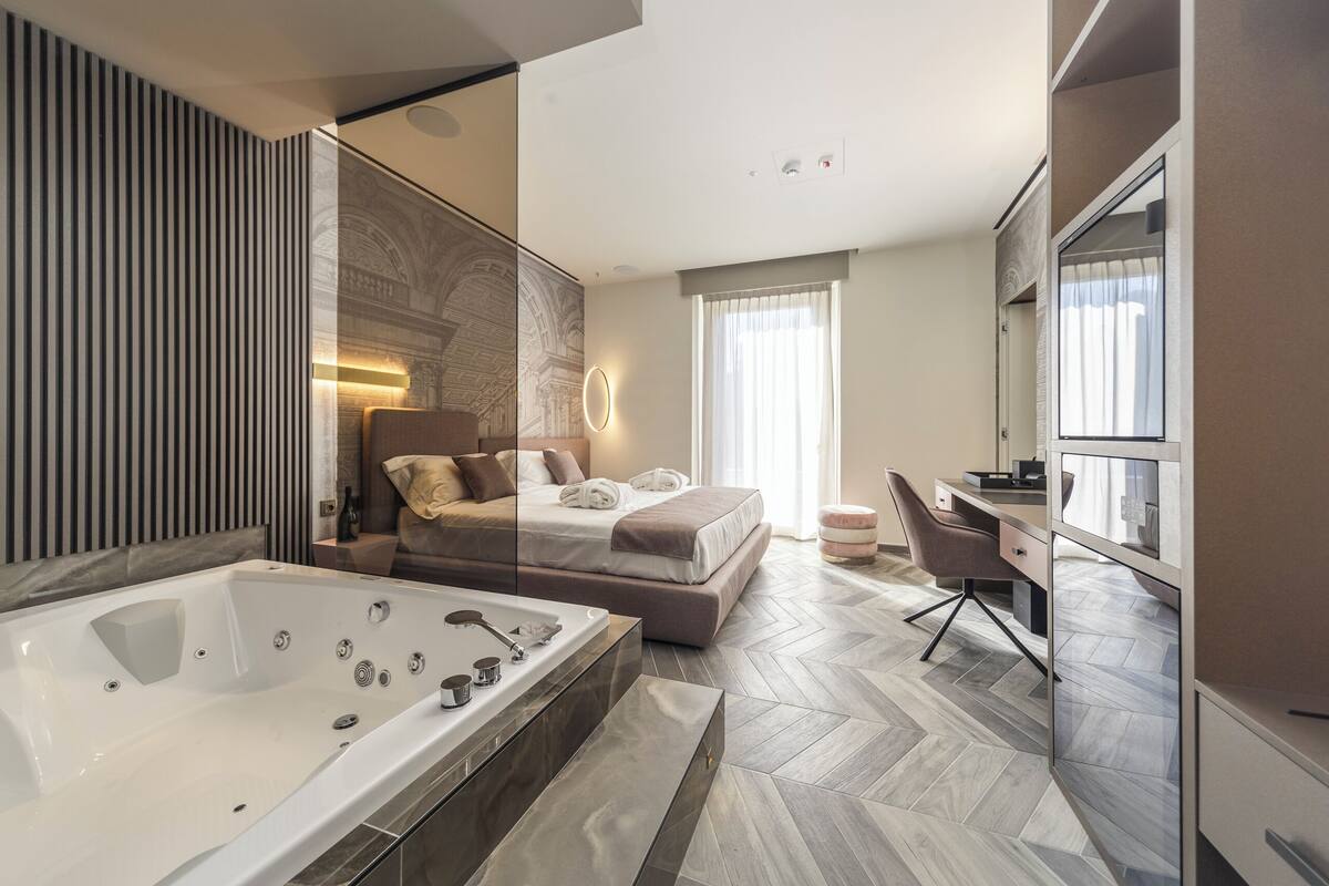 Une chambre moderne dotée d’un grand lit, d’un espace bureau séparé, d’un dressing et d’une grande salle de bain avec un jacuzzi.