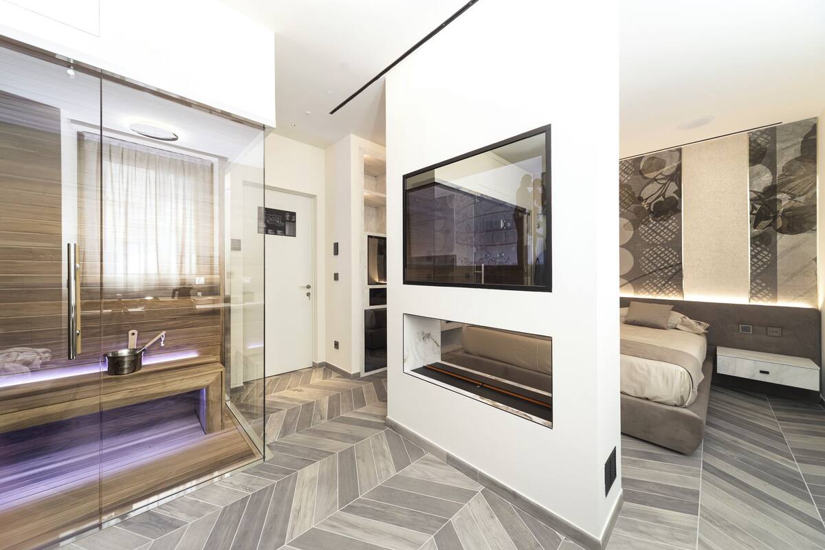 Une chambre moderne dotée d’une douche en verre, d’un banc intégré, d’un grand miroir et d’un lit avec une tête de lit.